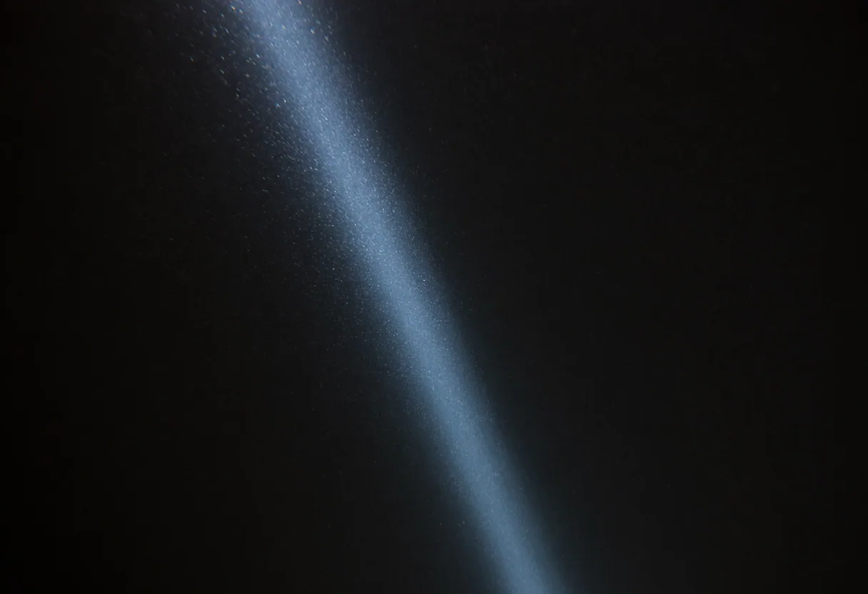 A single narrow blade of cold light descending into black water, catching suspended particles, with nothing else visible.